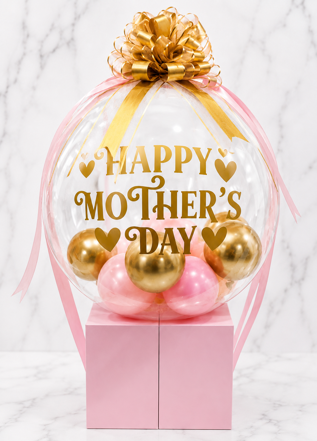Elegant pink and gold Mother’s Day bubble balloon arrangement with satin bow and luxury gift box base.