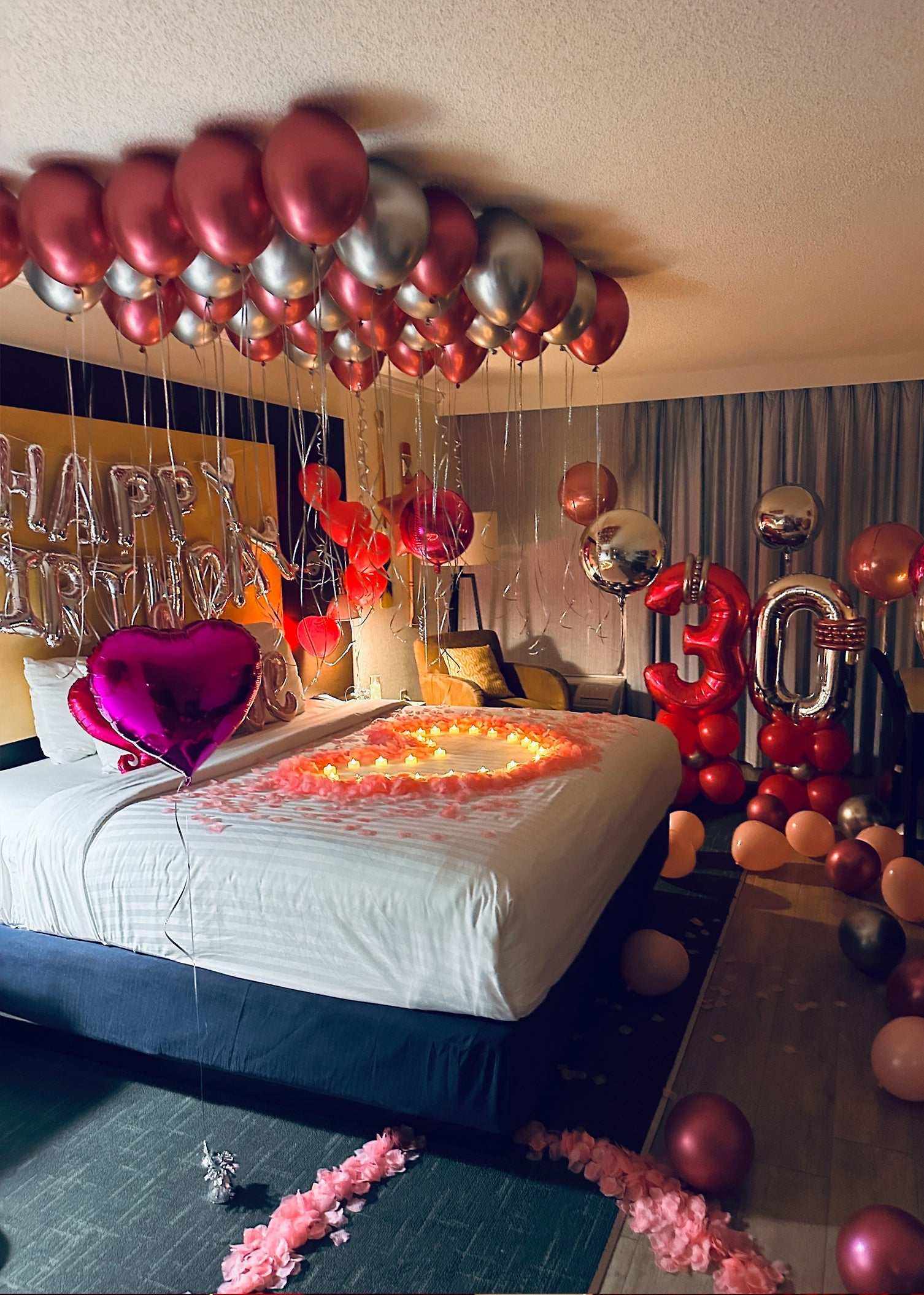 Pink Birthday Surprise Package hotel room decorated with balloons, rose petals, and LED lights for a romantic birthday celebration