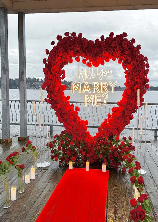 Heart-shaped floral arrangement with 'Will you marry me?' proposal at a waterfront location