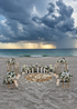 Classic beach proposal setup with luxury white floral arrangements, gold stands, LED candles, round rug and white rose petals