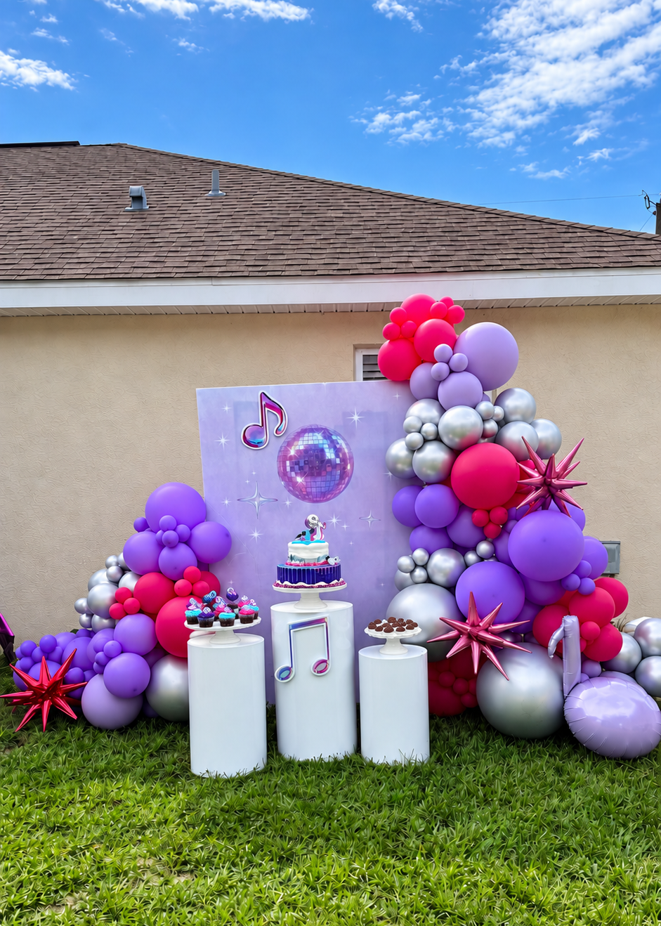 Custom K-pop birthday backdrop with pink, purple and silver balloon décor, character cutouts and white pedestals.