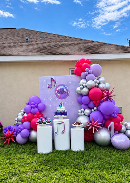Custom K-pop birthday backdrop with pink, purple and silver balloon décor, character cutouts and white pedestals.