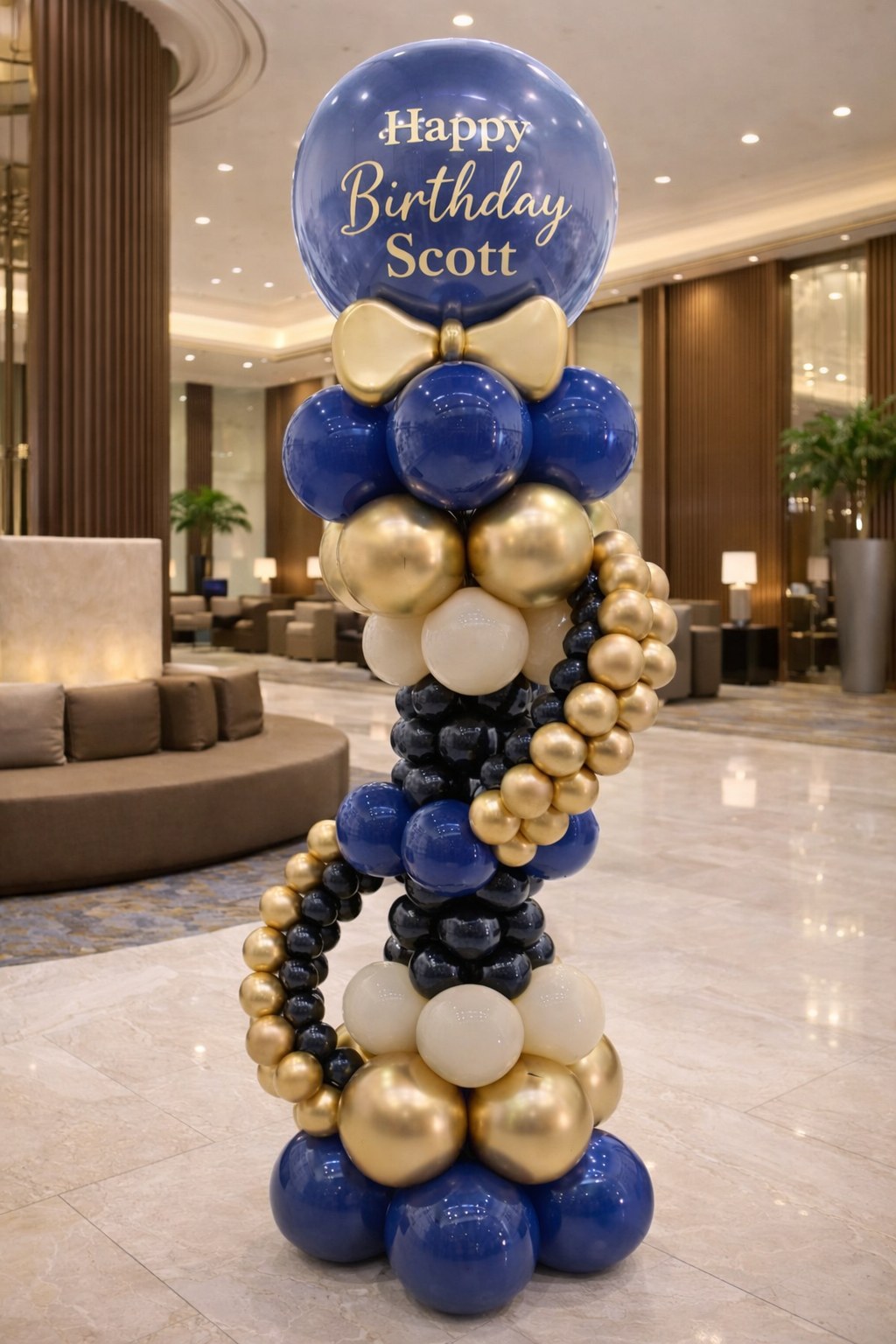 Luxury navy and gold balloon column with personalized bubble balloon reading Happy Birthday in elegant hotel lobby setup