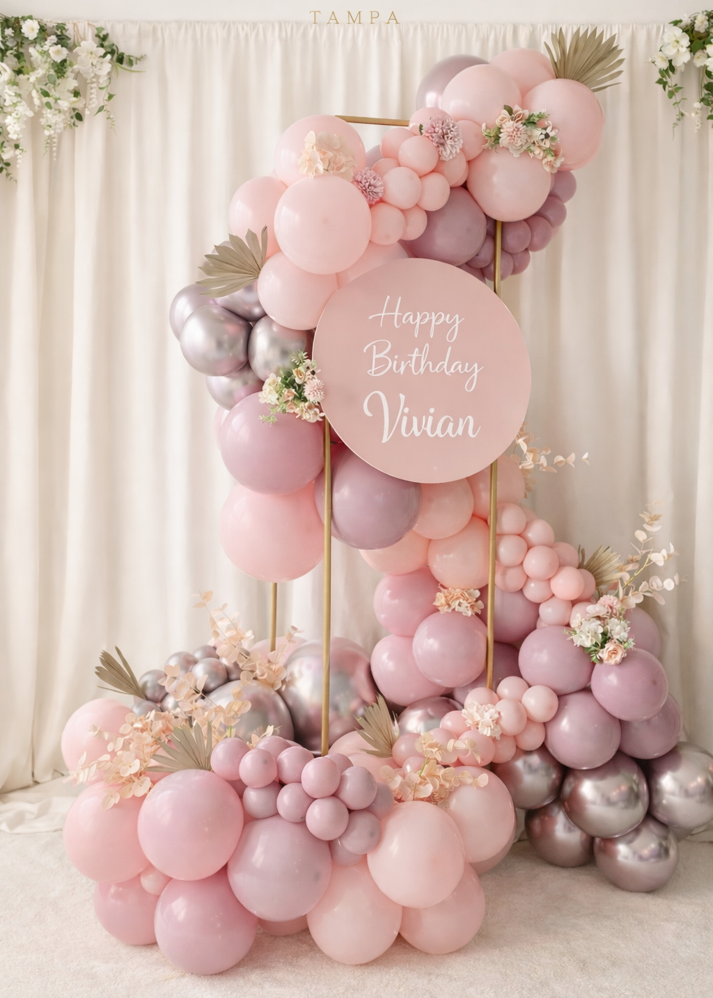 Luxury blush pink birthday balloon garland with custom sign and floral accents for elegant party backdrop