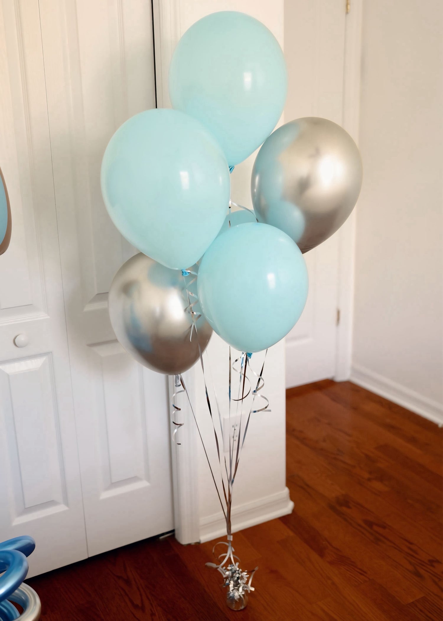 Bunch of light blue and silver balloons against a white wall.