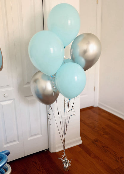 Bunch of light blue and silver balloons against a white wall.