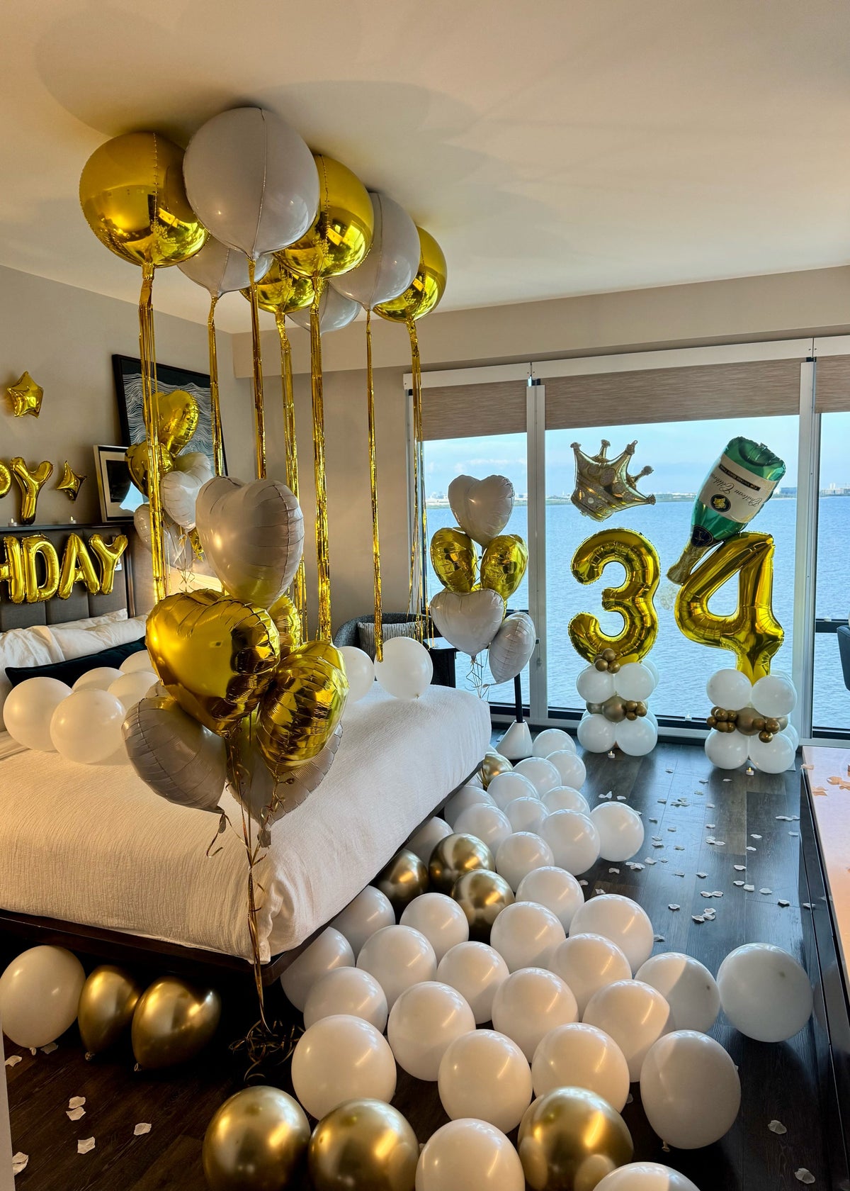 Luxury gold and white birthday room decorated with balloons, rose petals, and LED lights for a hotel surprise in Tampa