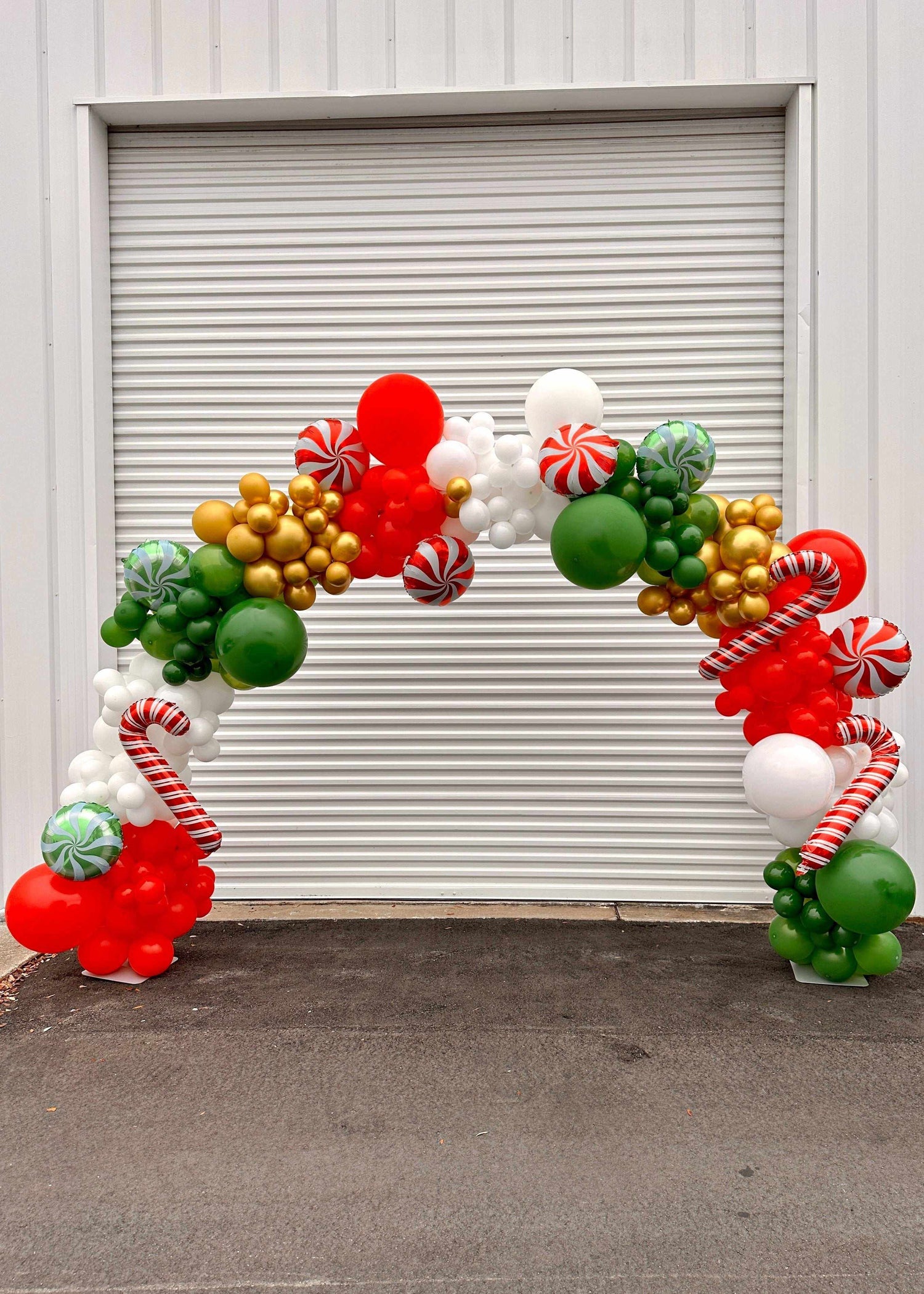 Festive designer and theme balloon arch with red, green, white, and gold balloons, candy cane decorations for event celebration